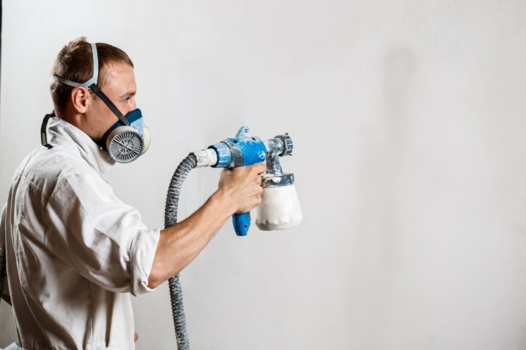 worker painting wall with spray gun white color e1690947615945